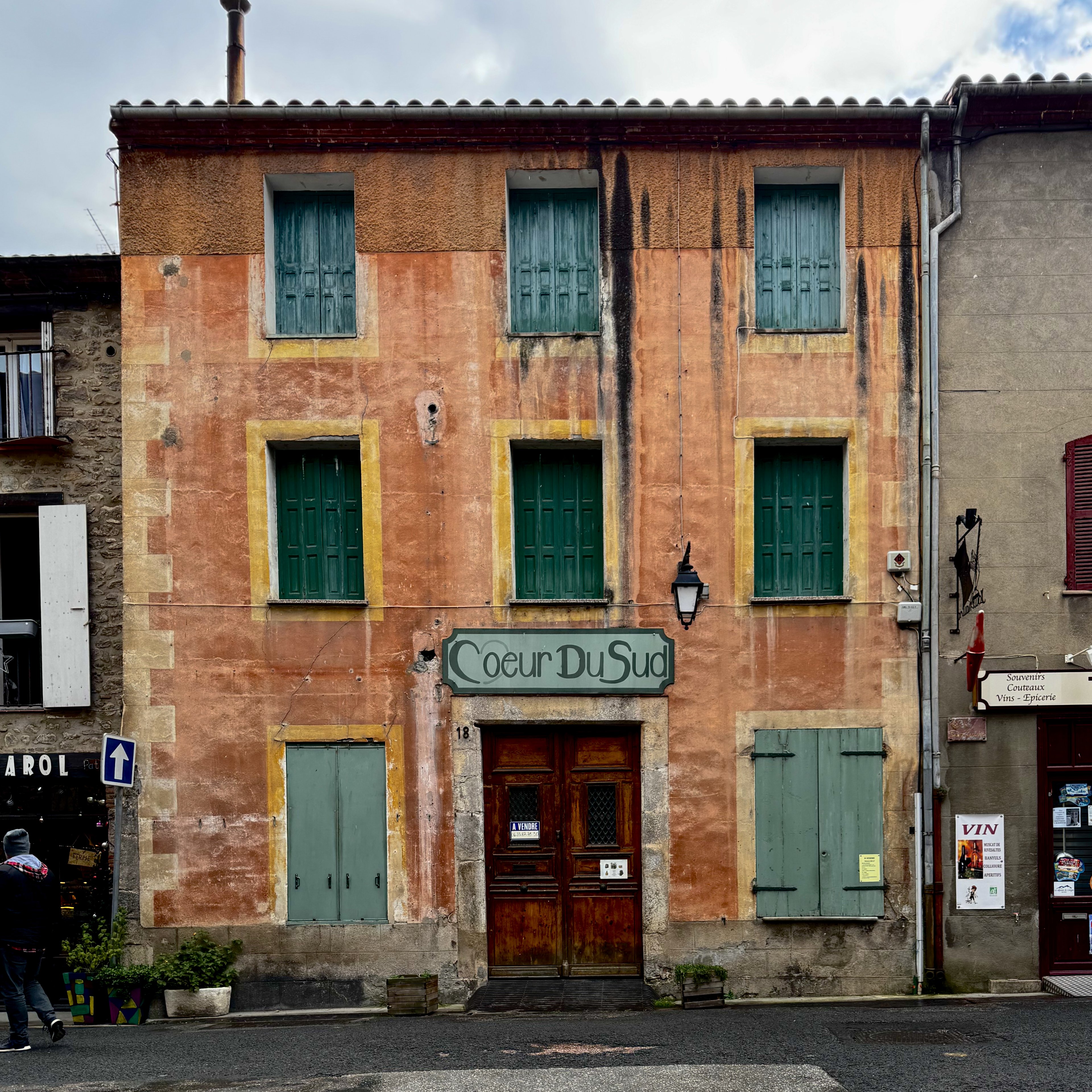 A weathered ochre shopfront with green shutters, Cœur du Sud over the door